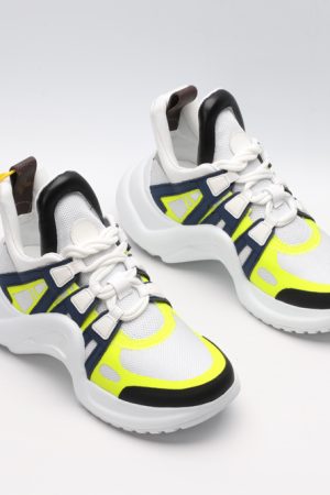 A pair of white chunky athletic sneakers with bold navy blue and neon yellow overlays