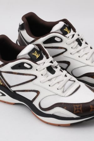 A pair of white athletic sneakers with brown monogram patterns on the toe and side